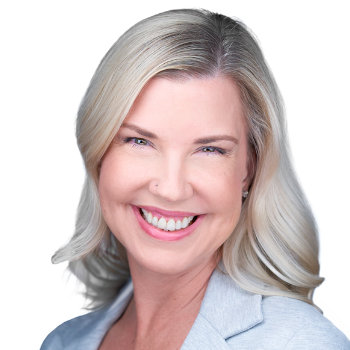 Smiling individual with long, light hair wearing a light-colored blazer on a plain background.