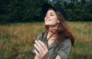 A person wearing a black cap smiles while standing in a grassy field with trees in the background.